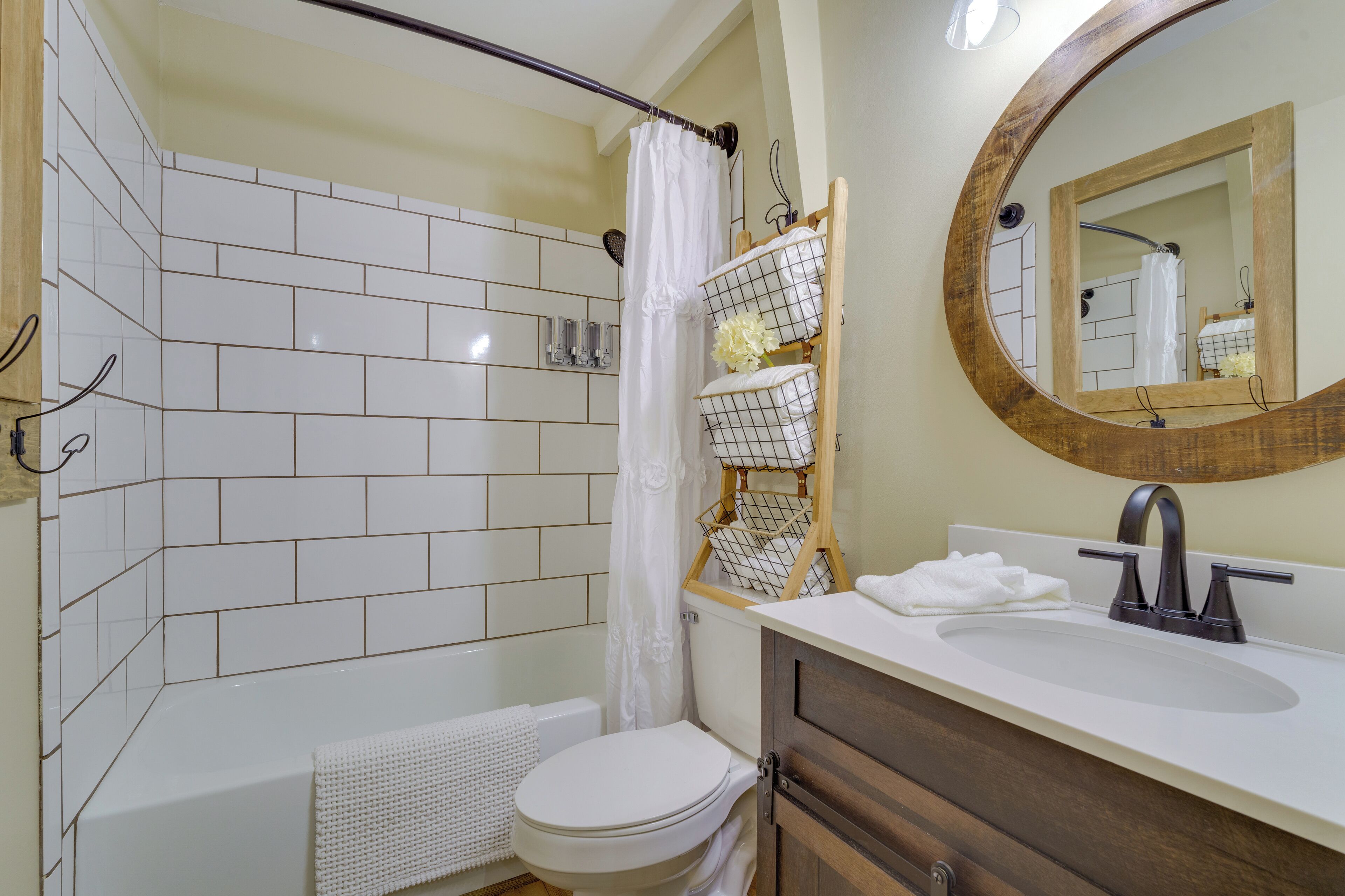 A bathroom with white tiled walls, a white toilet, a bathtub with a shower curtain, a wooden vanity with a sink, and a mirror with a wooden frame.