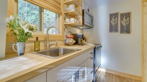 Une cuisine moderne dotée d’un grand îlot central, d’appareils électroménagers en acier inoxydable, d’étagères en bois et d’une fenêtre offrant une vue sur les arbres.