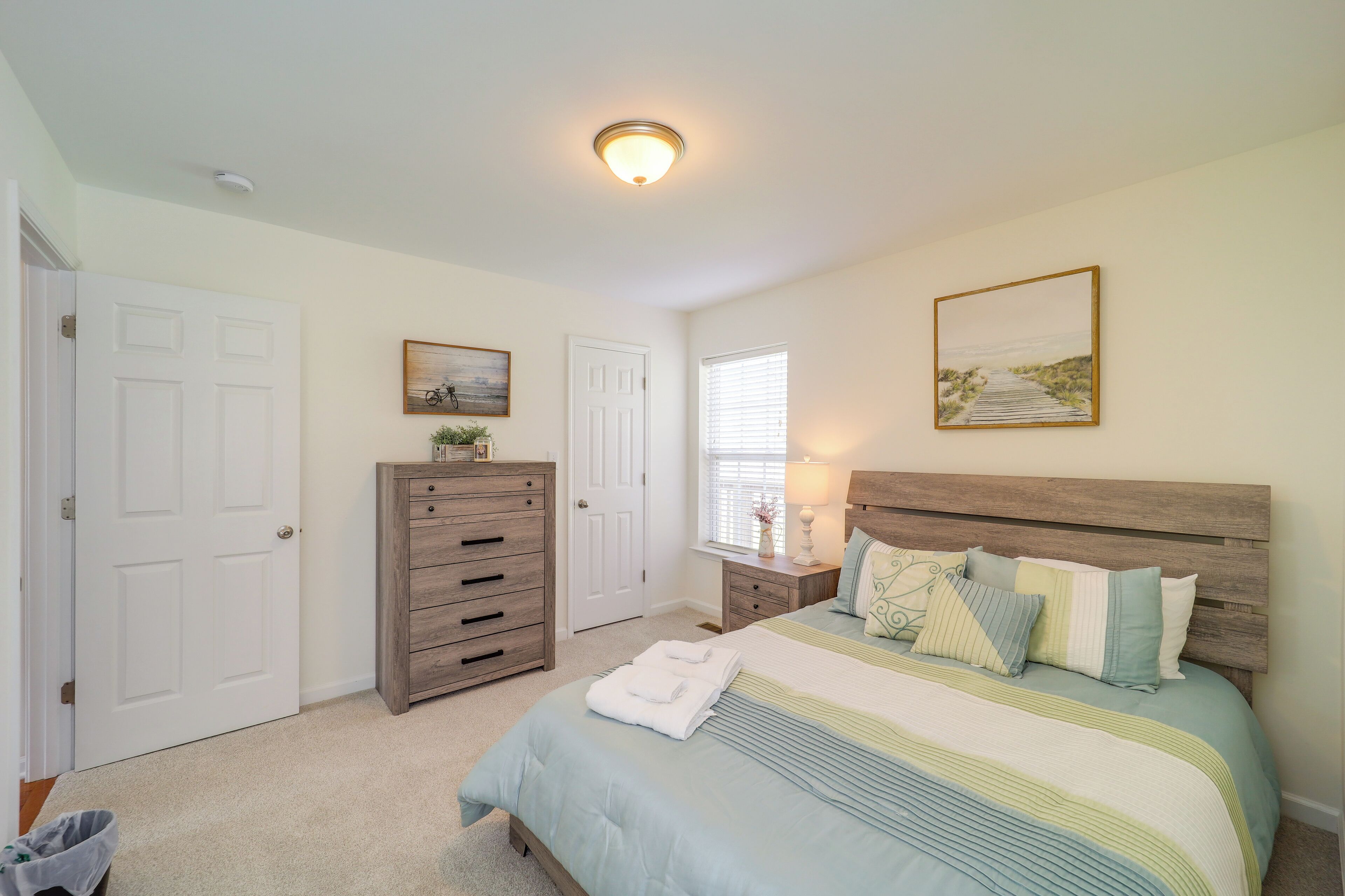 A bedroom with a bed, dresser, nightstand, and a window with blinds.