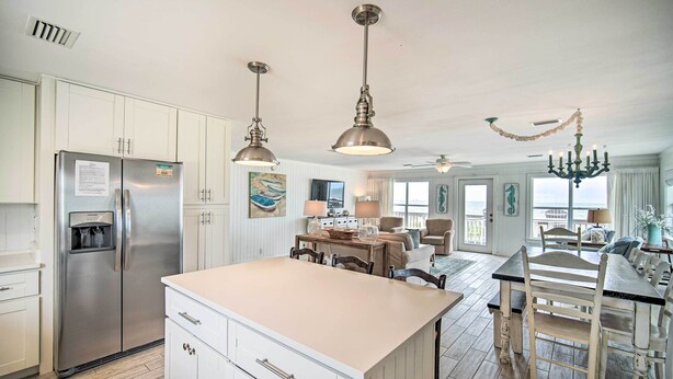 A spacious kitchen with a large island, stainless steel refrigerator, pendant lights, and a chandelier.