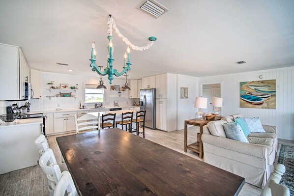 A modern kitchen with white cabinetry, a wooden dining table, and a teal chandelier. - Sunny Gulf Shores Haven, 3 Mi to Fort Morgan! (Gulf Shores)