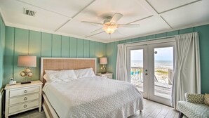 A bedroom with a bed, nightstands, a ceiling fan, and a view of the beach through a sliding door.