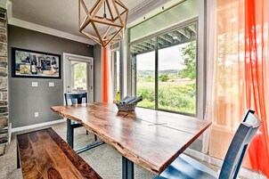 A dining area with a large wooden table, chairs, and a view through large windows.
