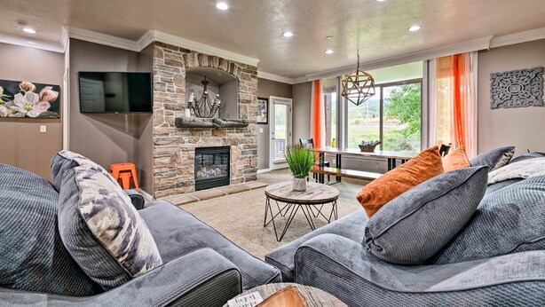 A living room with a stone fireplace, grey sofas, a flat-screen TV, and a dining area with orange curtains.