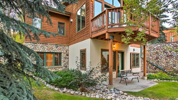 A two-story house with a stone facade, wooden deck, and a stone pathway leading to a bench. - Steamboat Springs Townhome: 1 Block to Ski Lifts! (Steamboat Springs)