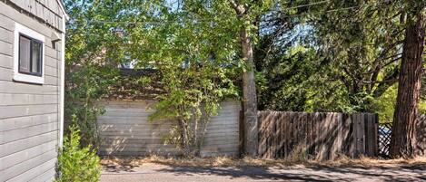 A residential property with a gravel driveway, wooden fence, and a small tree.