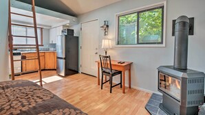 A compact living space with a kitchenette, a dining area with a table and chair, a wooden ladder, and a wood-burning stove. - Warm & Inviting Ashland Cottage < Half-mile to SOU (Ashland)