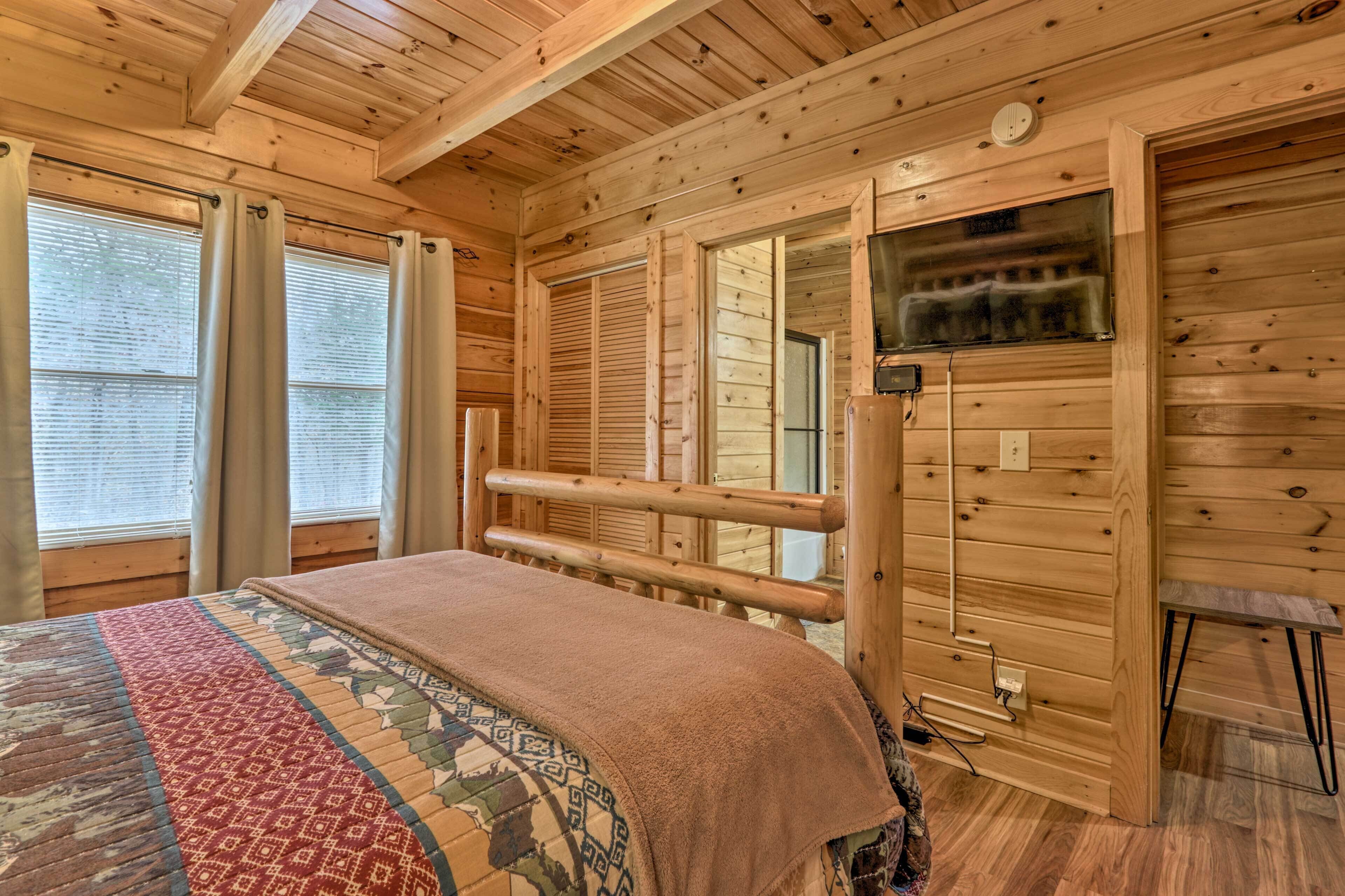 A wooden cabin room with a bed, a television, and a window with blinds.