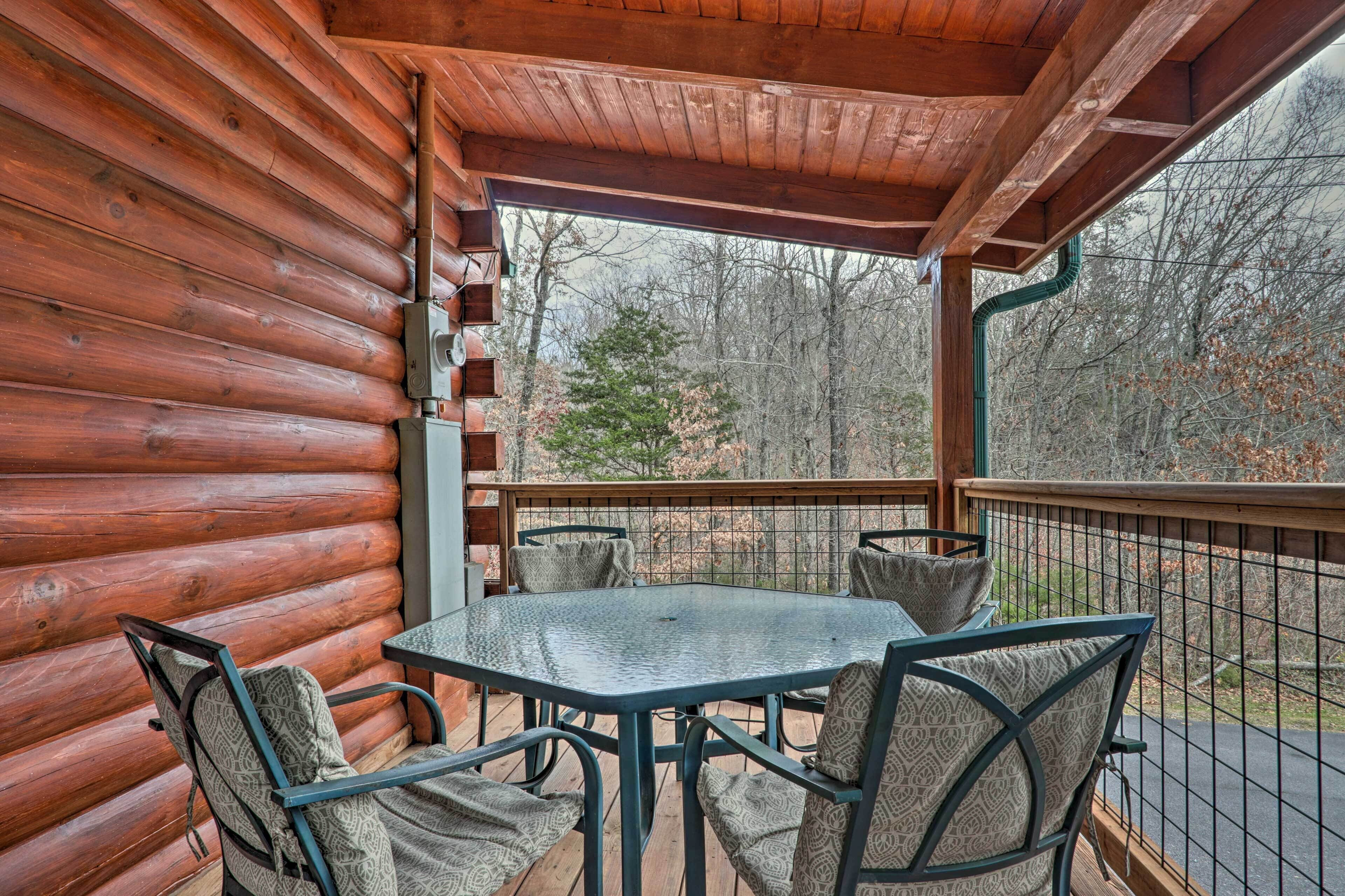 A wooden log cabin with a glass table and chairs on a balcony, overlooking a forested area.