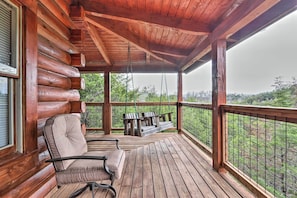 Um deck de madeira com uma cadeira de balanço e um banco, com vista para uma paisagem arborizada.