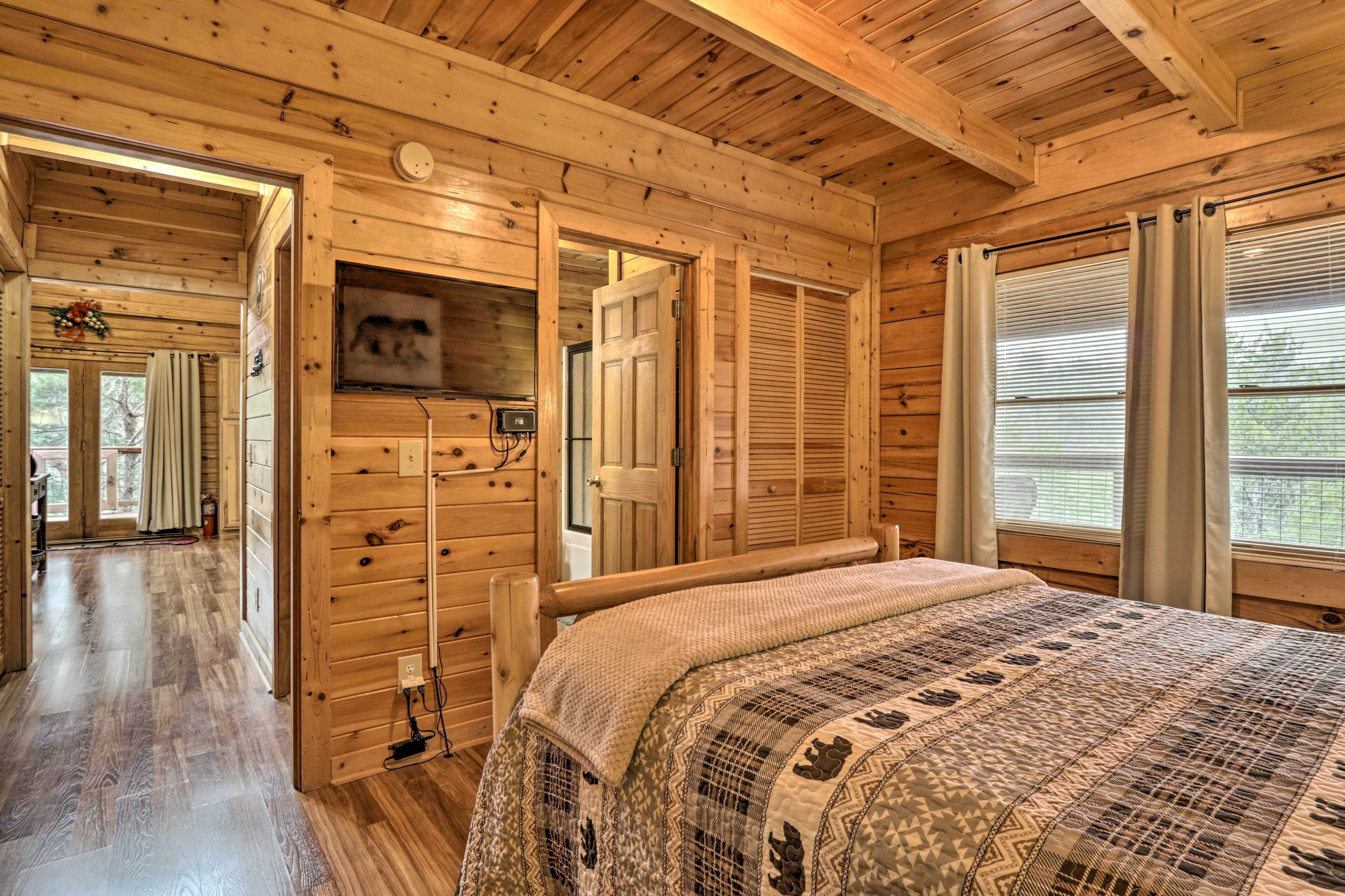 A wooden cabin interior with a bed, a television, and a door leading to another room.