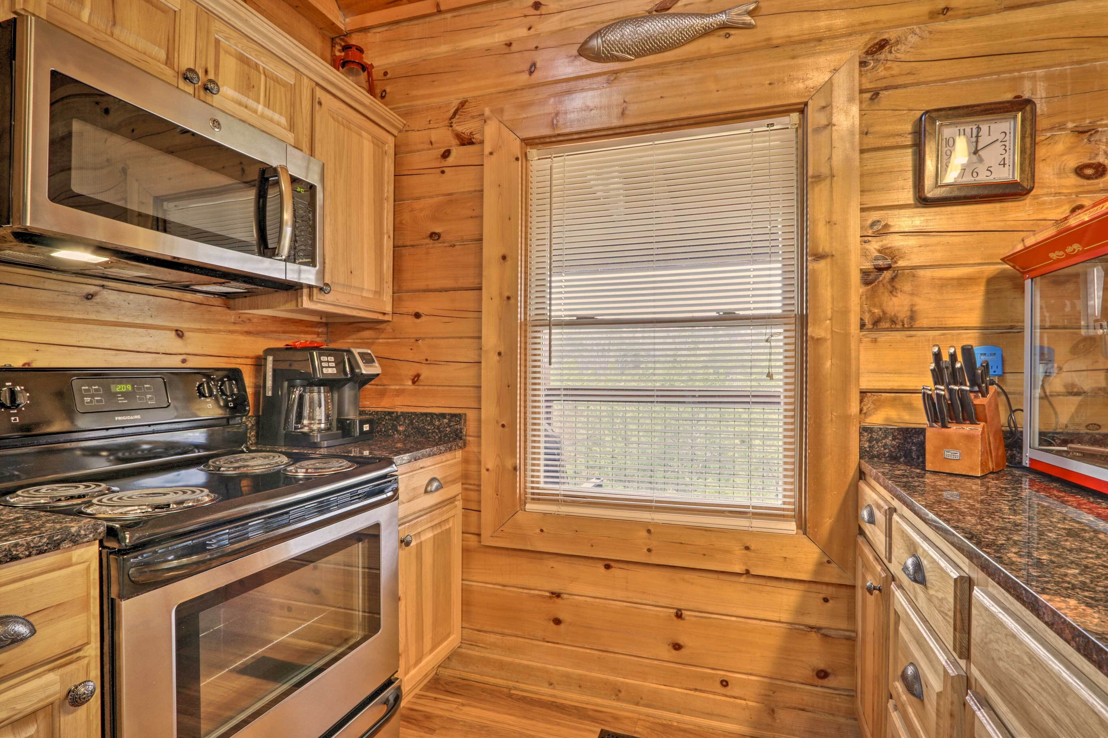A kitchen with wooden walls, a microwave, stove, oven, and a window with blinds.