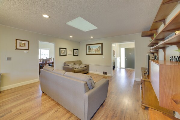 A spacious living room with hardwood floors, a grey sofa, and wooden shelving.