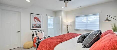 Une chambre à coucher avec un lit, un ventilateur de plafond, une fenêtre avec des stores, une porte et un tableau encadré au mur.