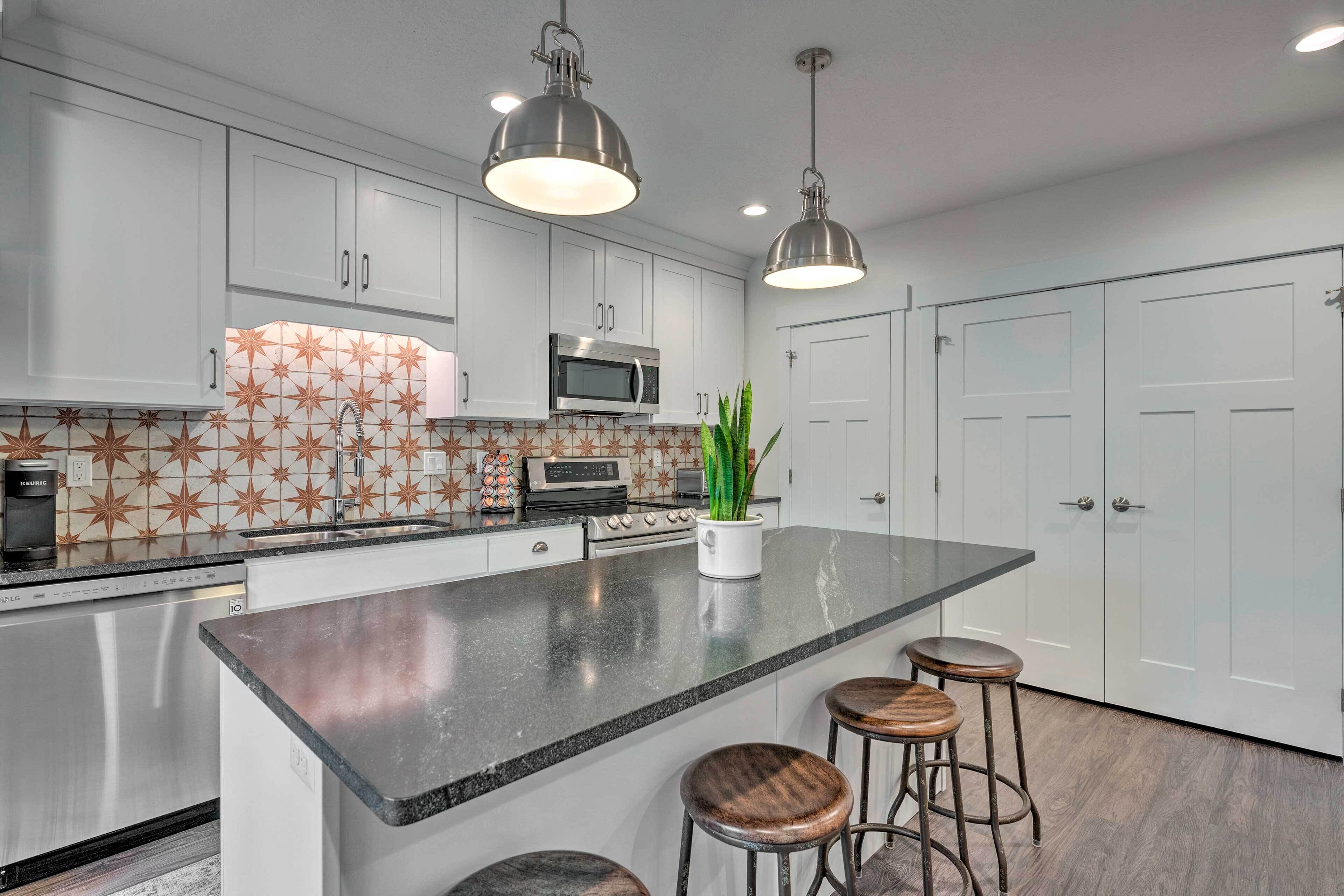 A modern kitchen with white cabinets, a large island with stools, a microwave, and pendant lighting.