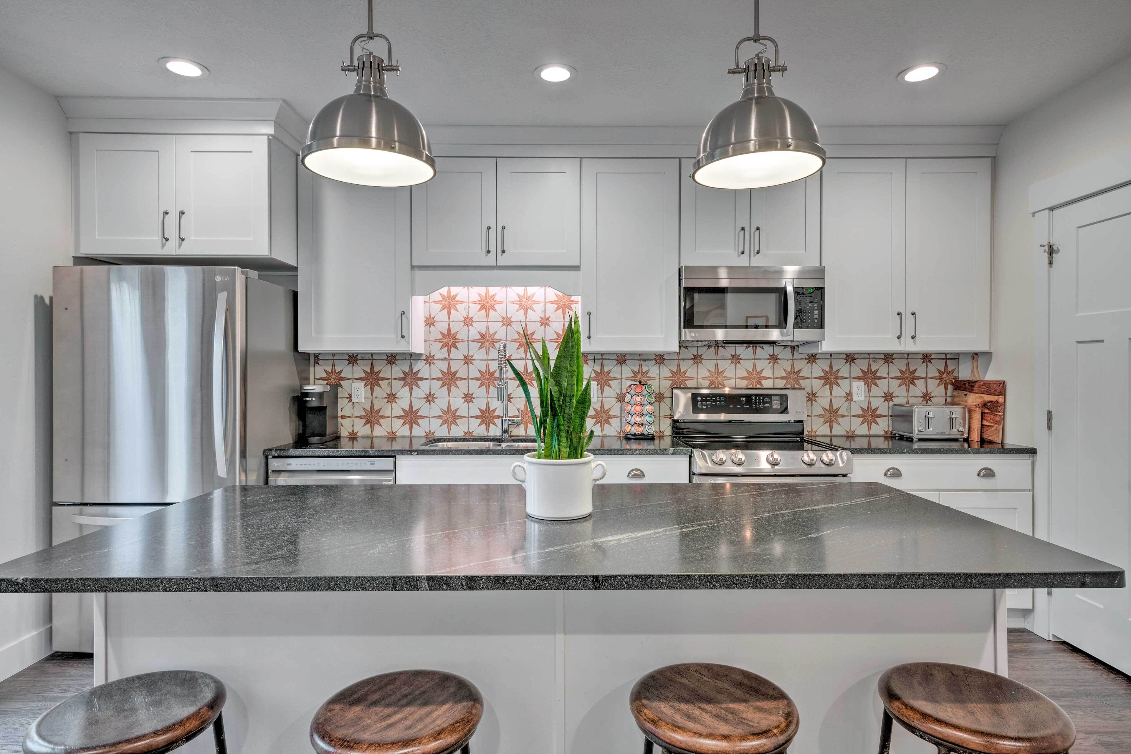 A modern kitchen with white cabinets, stainless steel appliances, a granite countertop, and two pendant lights.