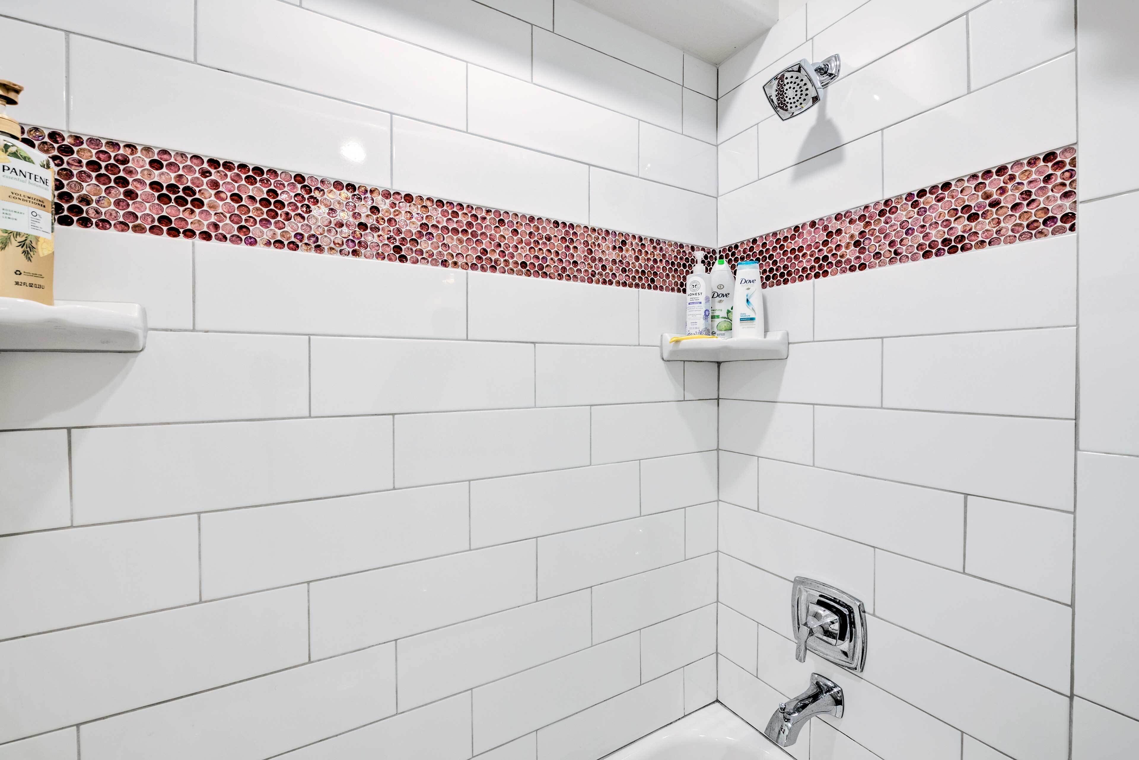 Un baño con azulejos blancos, un borde de mosaico rojo, una ducha y un inodoro.