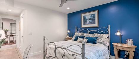 A bedroom with a bed, a ceiling fan, a bedside table with a lamp, and a framed picture on the wall.