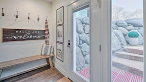 A hallway with a bench, a welcome sign, framed artwork, and a door leading to a rock garden. - Vibrant Chic Home ~ 20 Mi to Salt Lake City! (Draper)