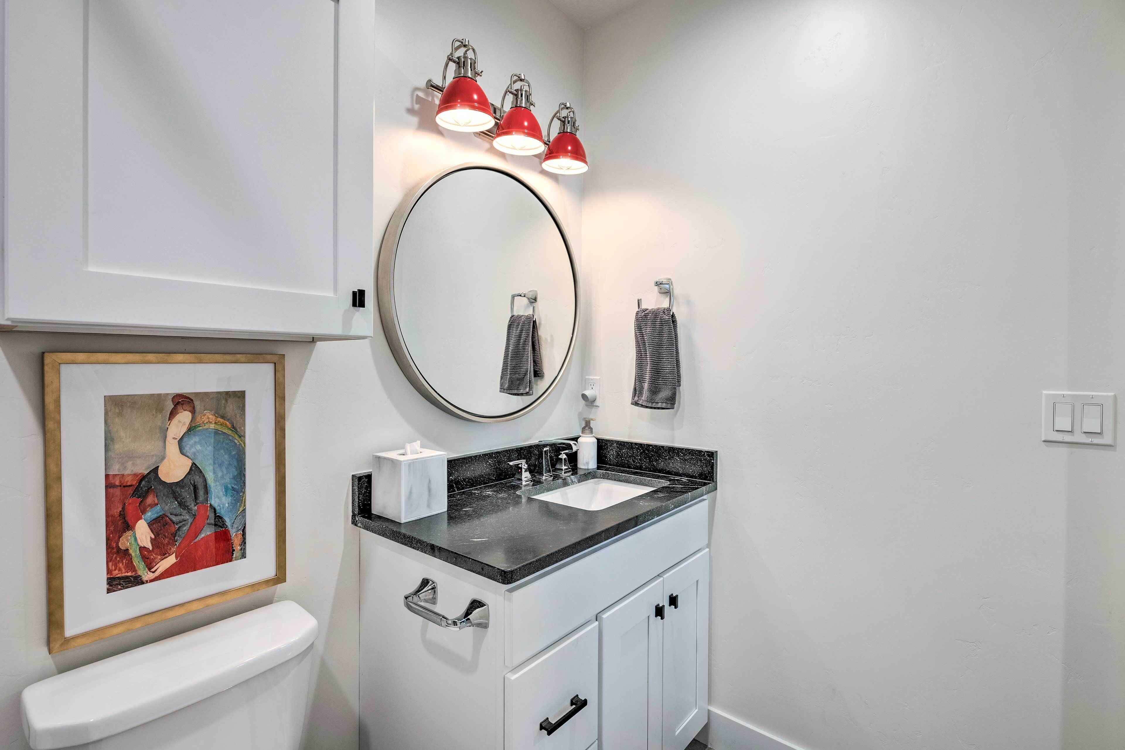 Une salle de bain avec un meuble-lavabo blanc, un miroir rond, un plan de toilette noir et des appliques murales rouges.
