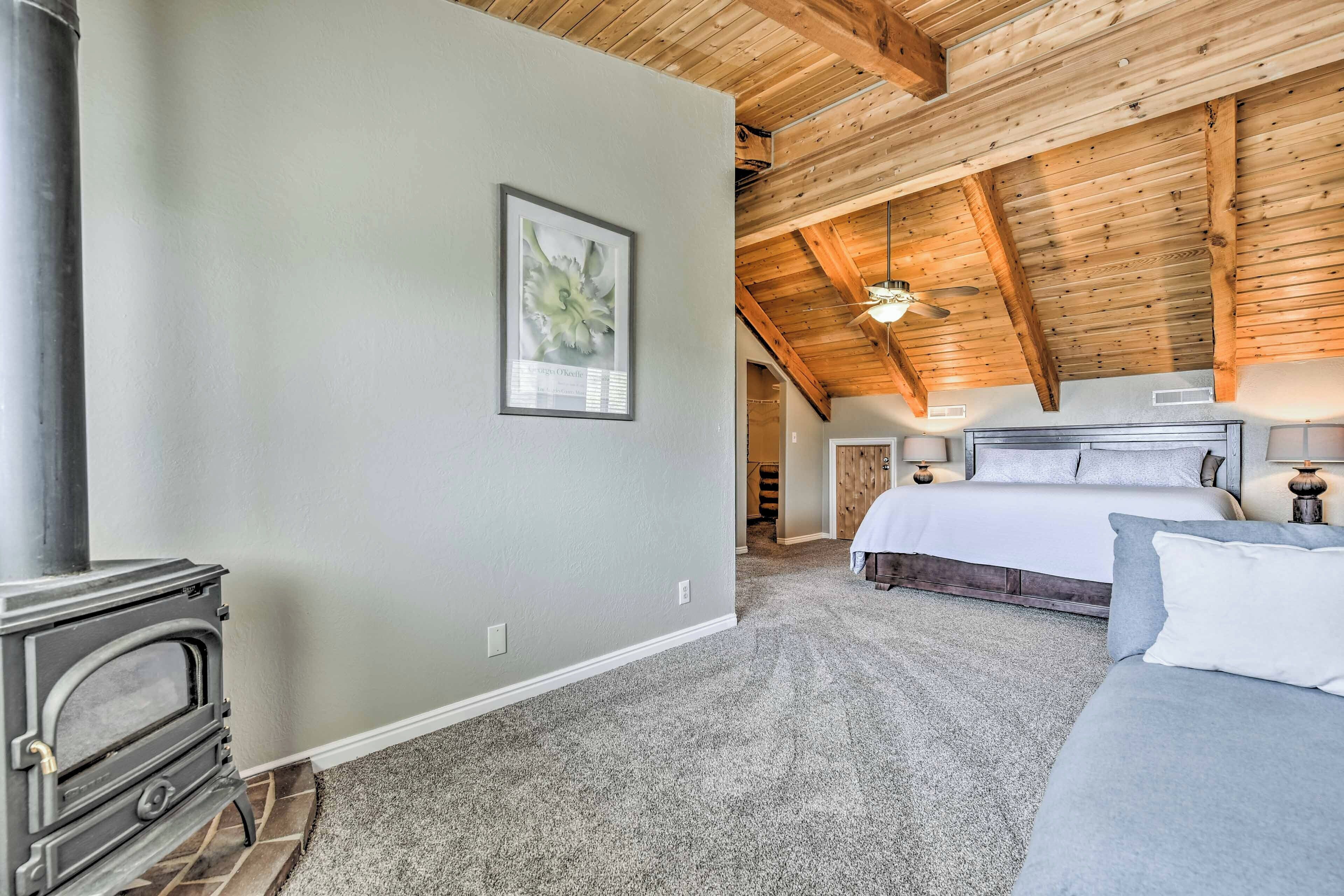 A bedroom with a large bed, a wooden ceiling, a fireplace, and a framed picture on the wall.