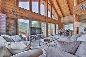 A spacious living room with a fireplace, large windows, and a television. - Spacious Hilltop Cabin w/ Deck & Scenic Views! (Eden)