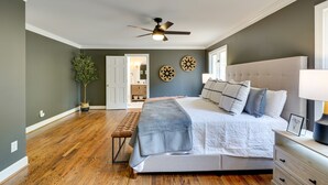 A bedroom with a large bed, a ceiling fan, wooden flooring, a bench, and a door leading to another room. - Spacious Waterfront Hyco Lake Retreat w/ Dock! (Leasburg)