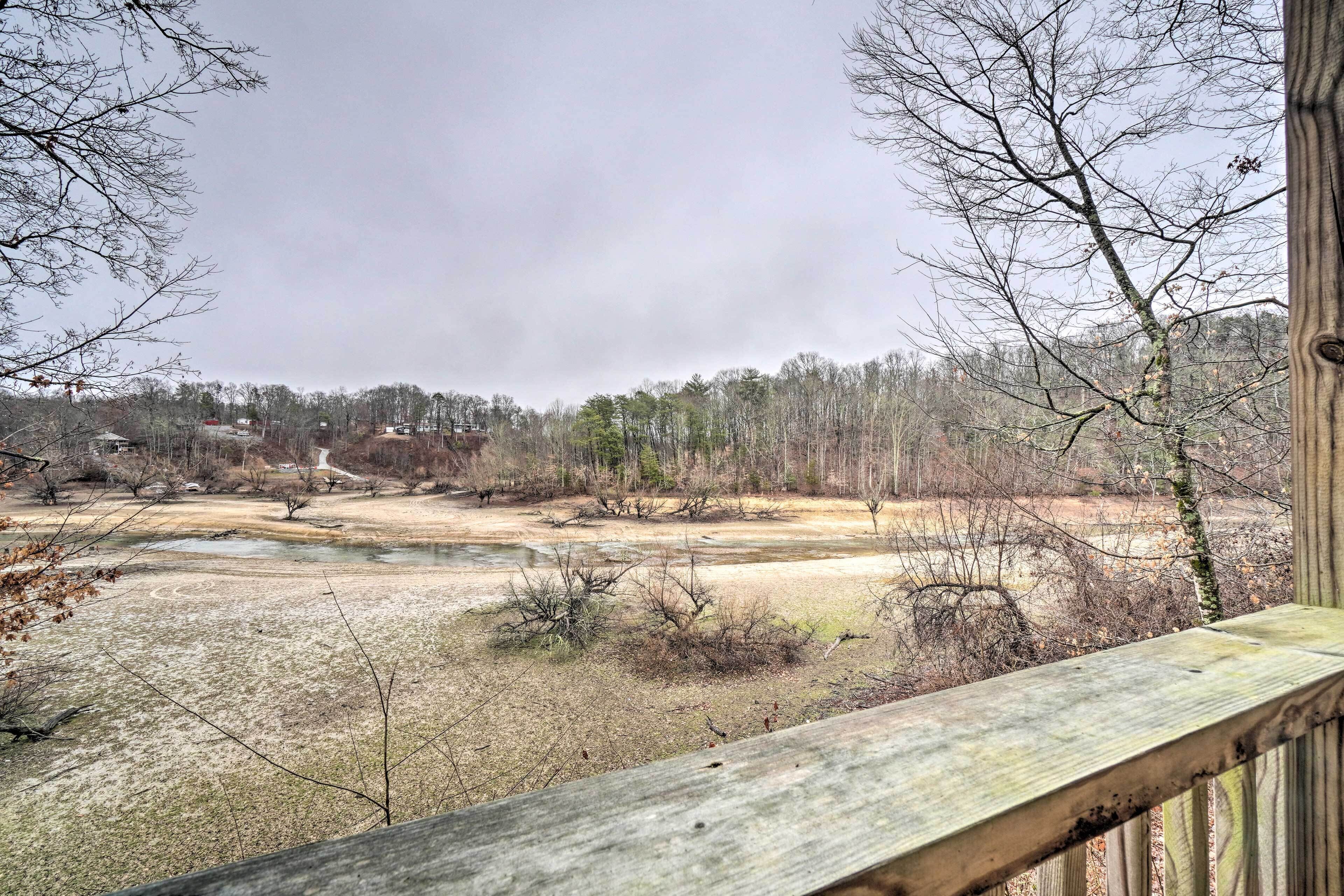 A view from a wooden deck overlooking a natural landscape with a river, trees, and a distant path.