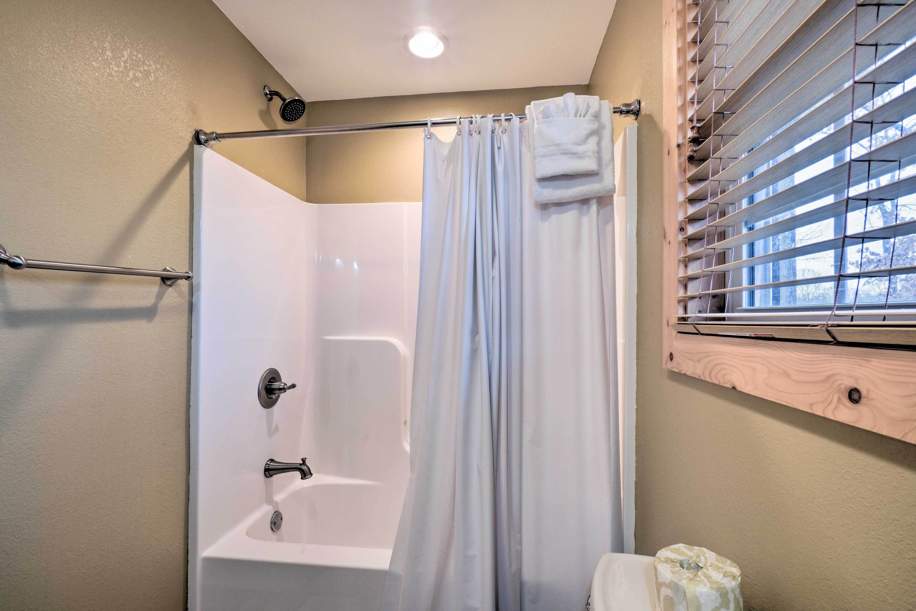 A bathroom with a shower, a bathtub, and a window with blinds.