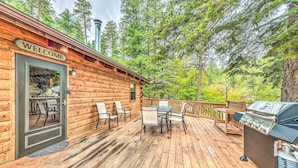 En stuga byggd av trä med en skylt som säger ”VÄLKOMMEN”, en veranda med utemöbler och en grill.