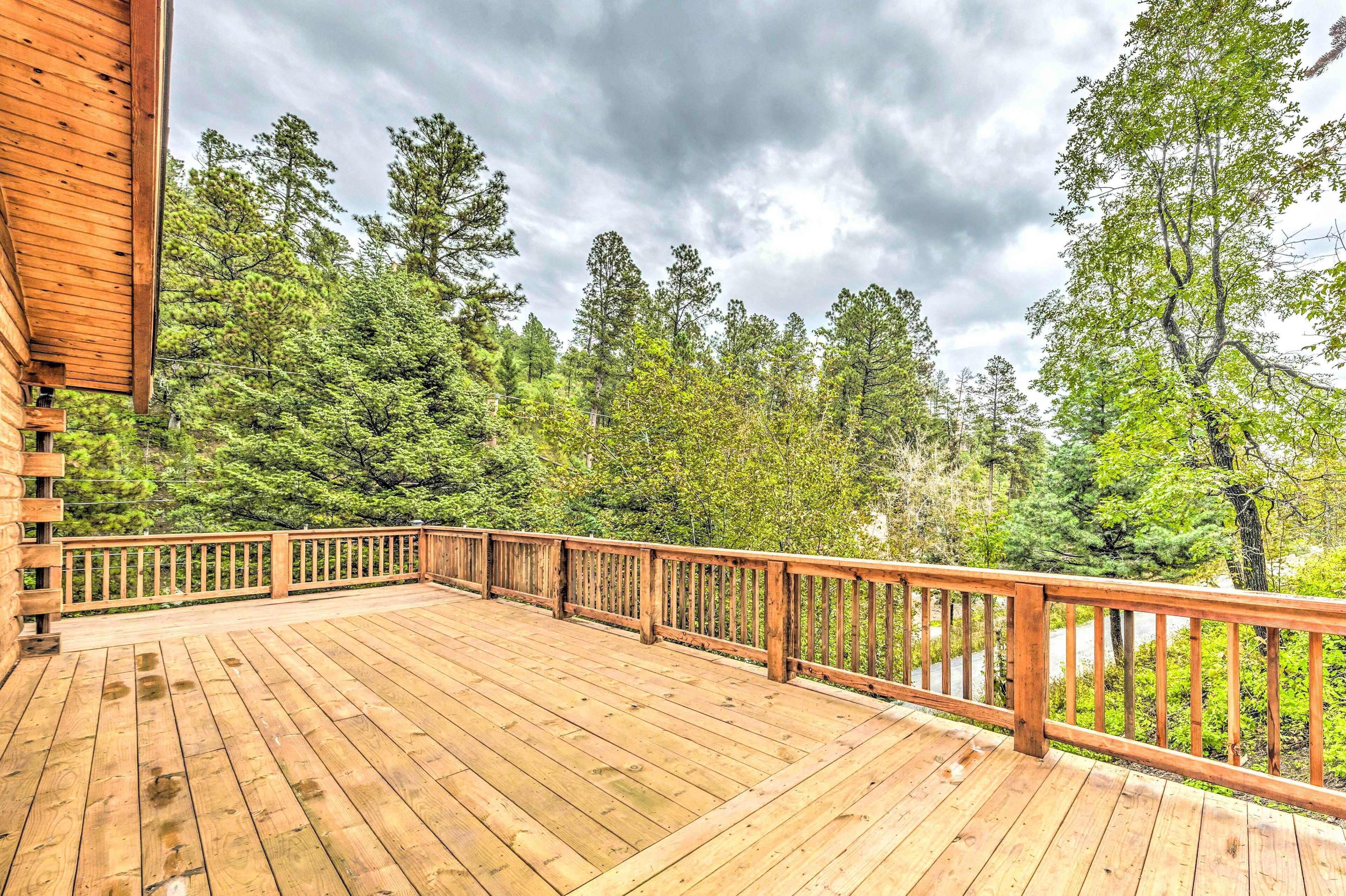 A wooden deck with a railing, surrounded by dense forest.