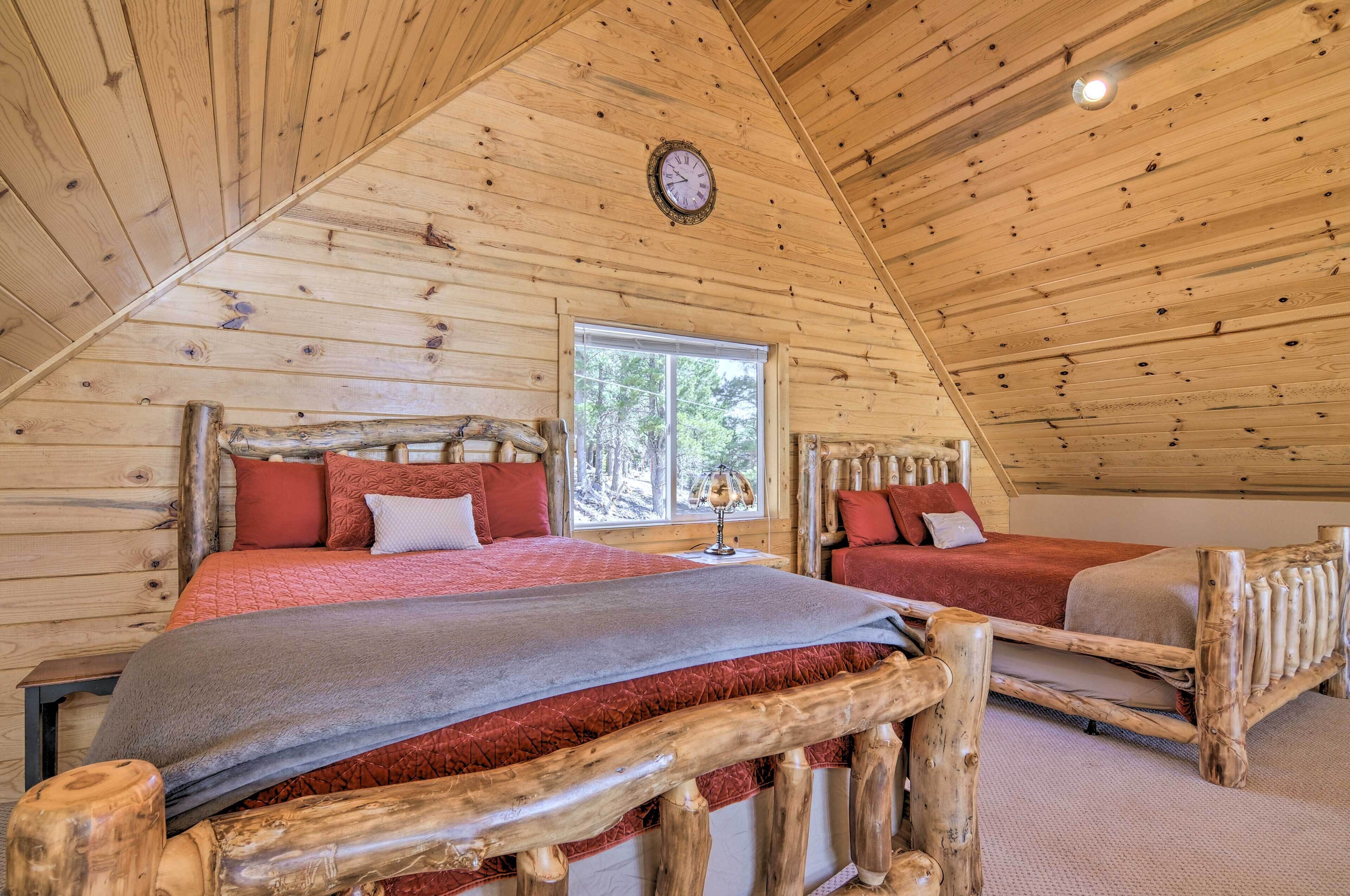 A log cabin bedroom with two beds, a wooden ceiling, and a window with a view of trees.
