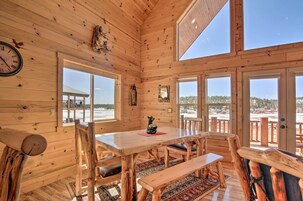 A wooden cabin interior with a dining table, benches, and large windows offering a view of a snowy landscape.