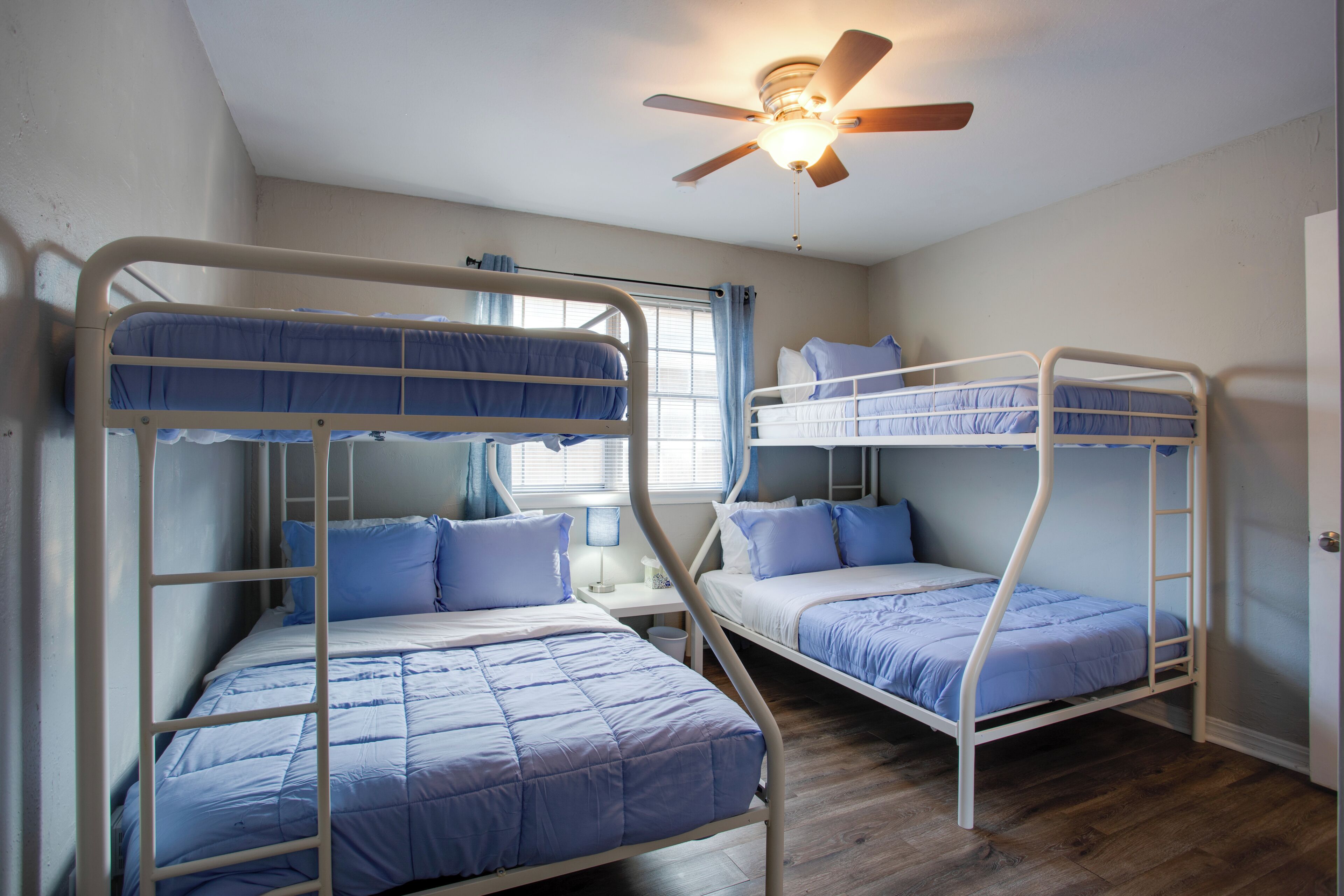A room with bunk beds, a ceiling fan, and a window with curtains.