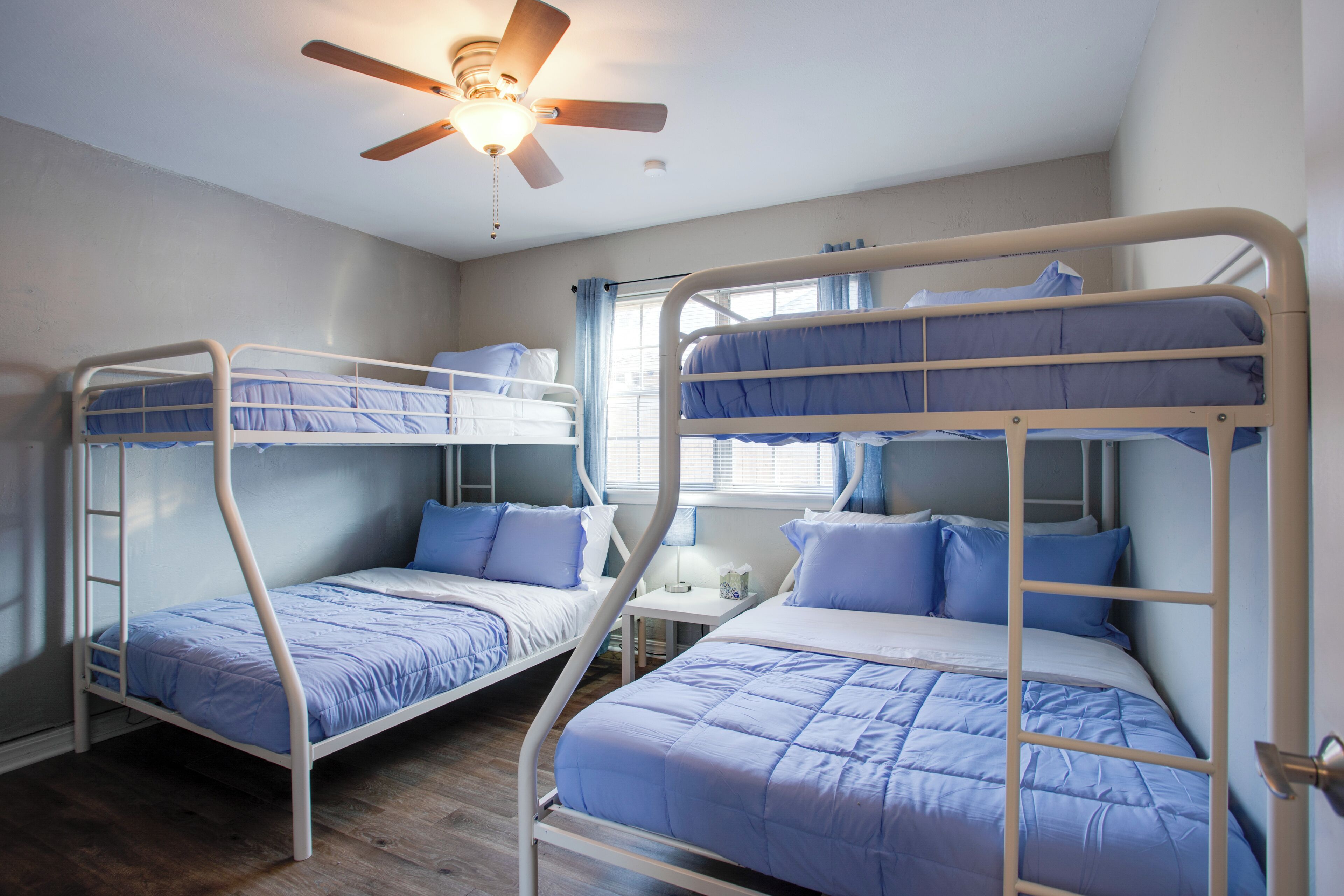 Un dormitorio con dos literas, un ventilador de techo y una ventana con cortinas.