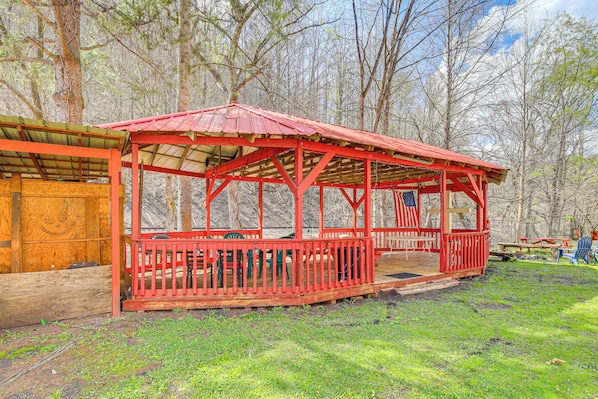 Un pavillon rouge doté d’un espace de repos couvert et d’une terrasse en bois, le tout entouré d’arbres.