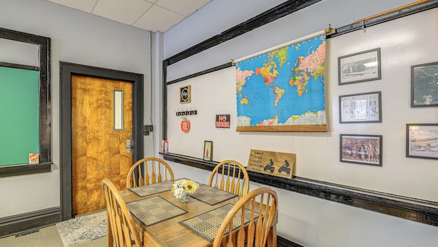 Un comedor con una mesa de madera, sillas, un mapa del mundo, cuadros enmarcados y un letrero de 'No Fumar'.