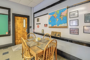 Un coin repas avec une table en bois, des chaises, une carte du monde, des photos encadrées et un panneau «
Il est interdit de fumer
».