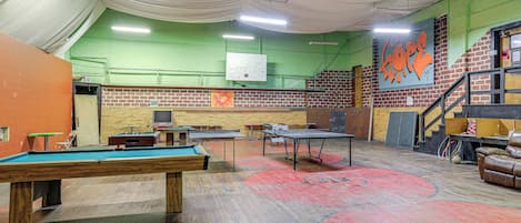 A billiards room with tables, a pool table, and a brick wall with graffiti.