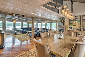 A spacious living area with a large wooden dining table, comfortable seating, and large windows offering views of the outdoors. - Stunning Enfield Home w/ Deck & Boat Dock! (Enfield)