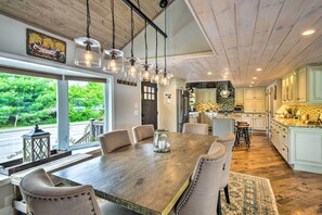 Un vaste espace dédié à la salle à manger, avec une grande table en bois, de nombreuses chaises et des luminaires suspendus.