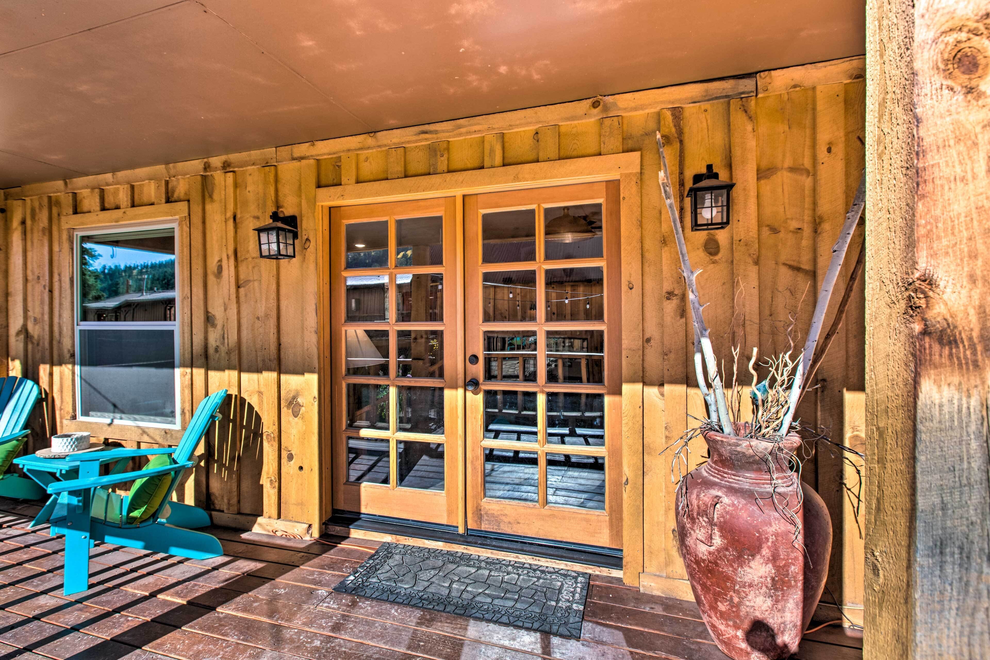 L’entrée d’un chalet en bois est dotée d’une porte coulissante en verre, de deux fauteuils Adirondack et d’une grande plante en pot.