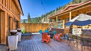 Una terraza de madera con mobiliario exterior, un muro de piedra y vistas a montañas.