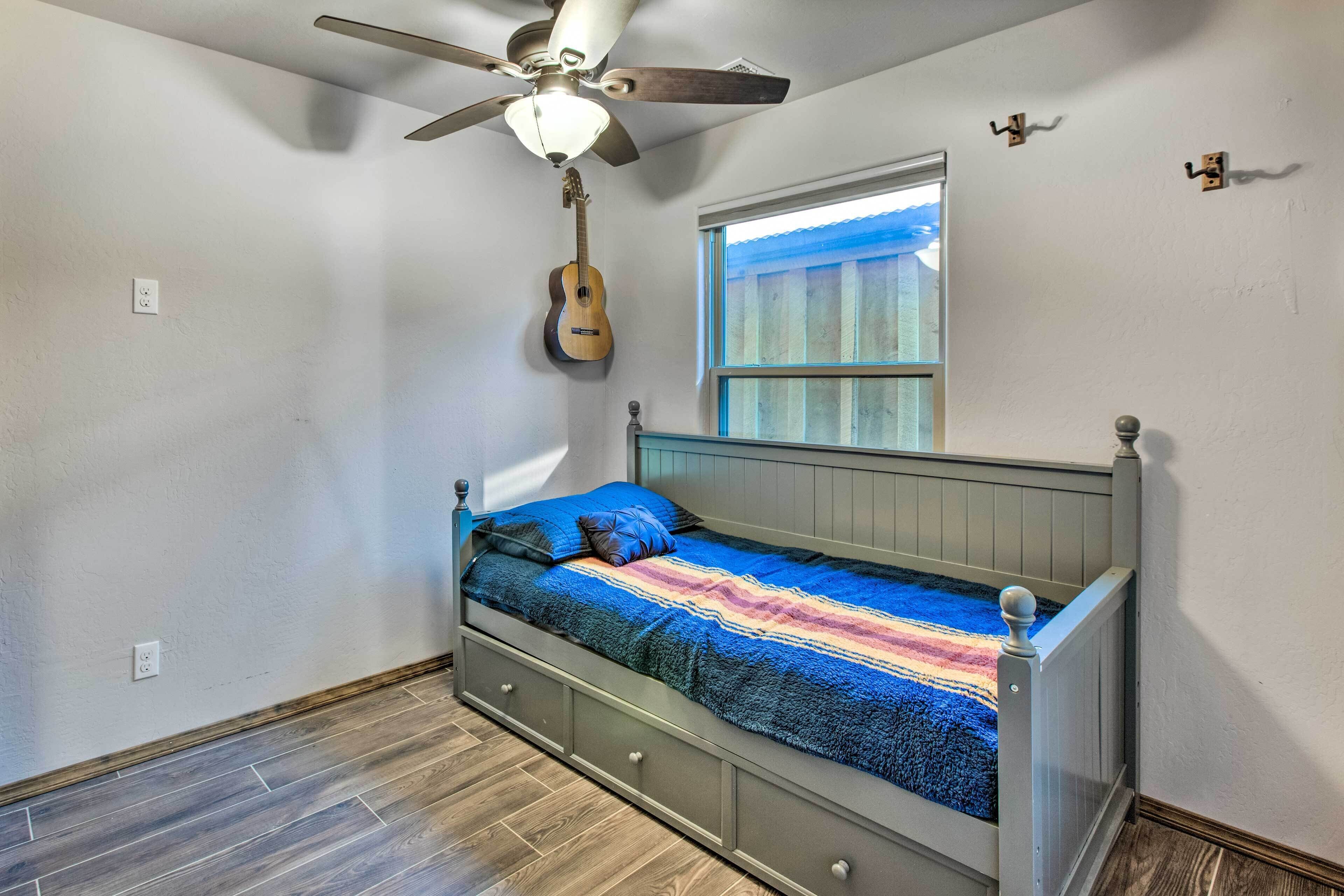 Une chambre à coucher avec un lit, un ventilateur de plafond, une fenêtre et une guitare accrochée au mur.