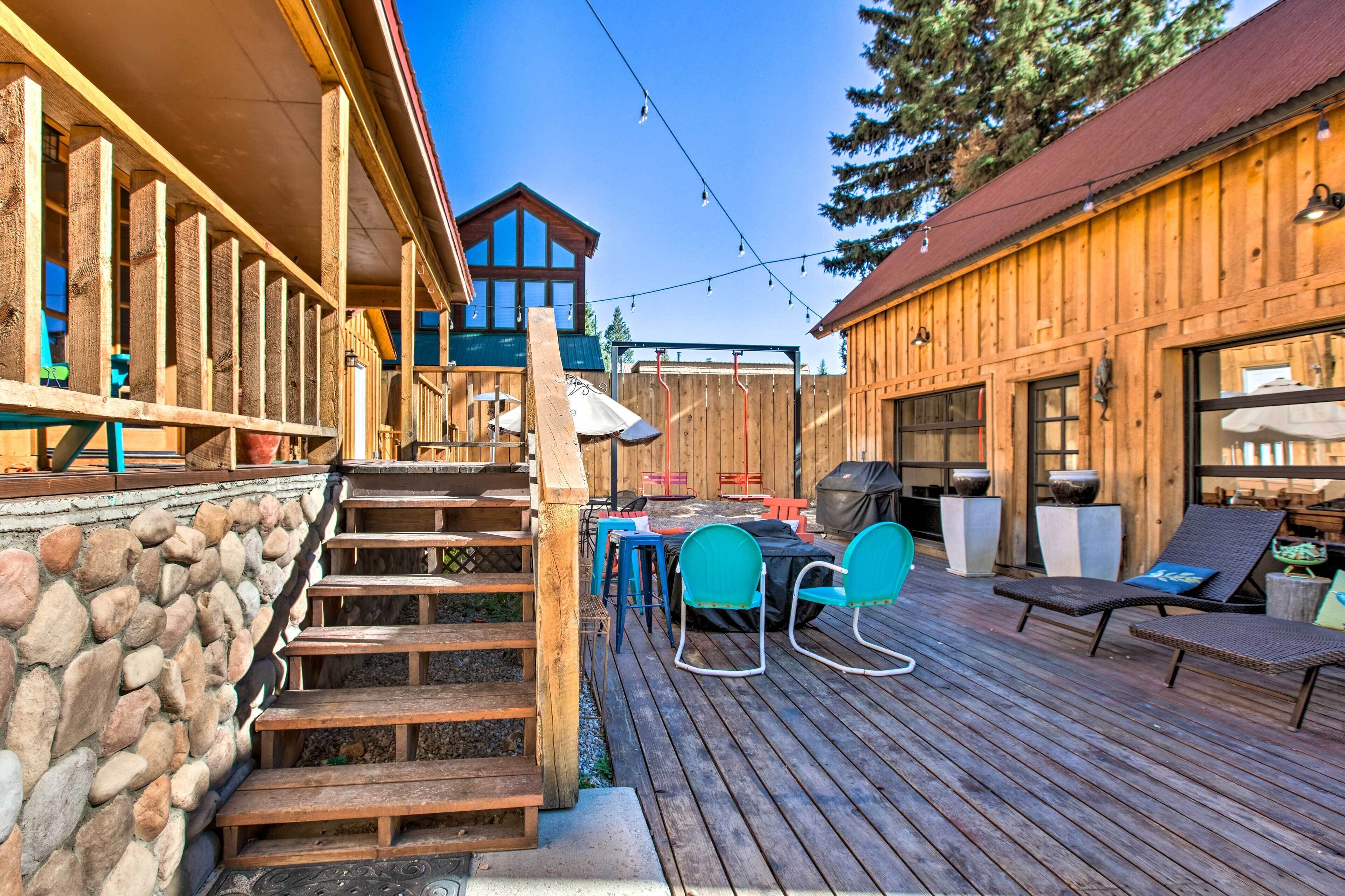 A wooden deck with outdoor seating, a stone wall, and a wooden building with large windows.