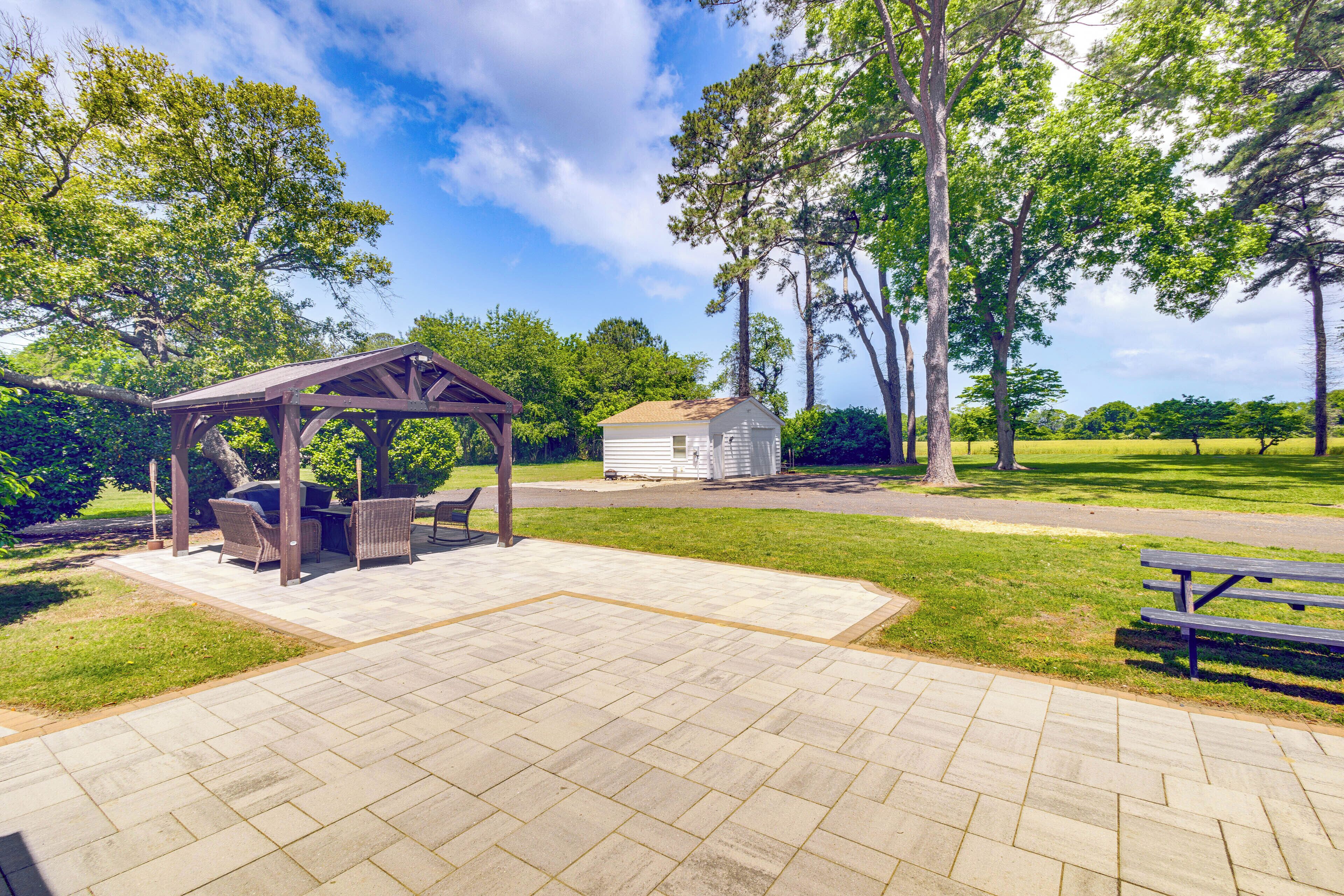 A gazebo with outdoor furniture, a small shed, and a picnic table in a park setting.