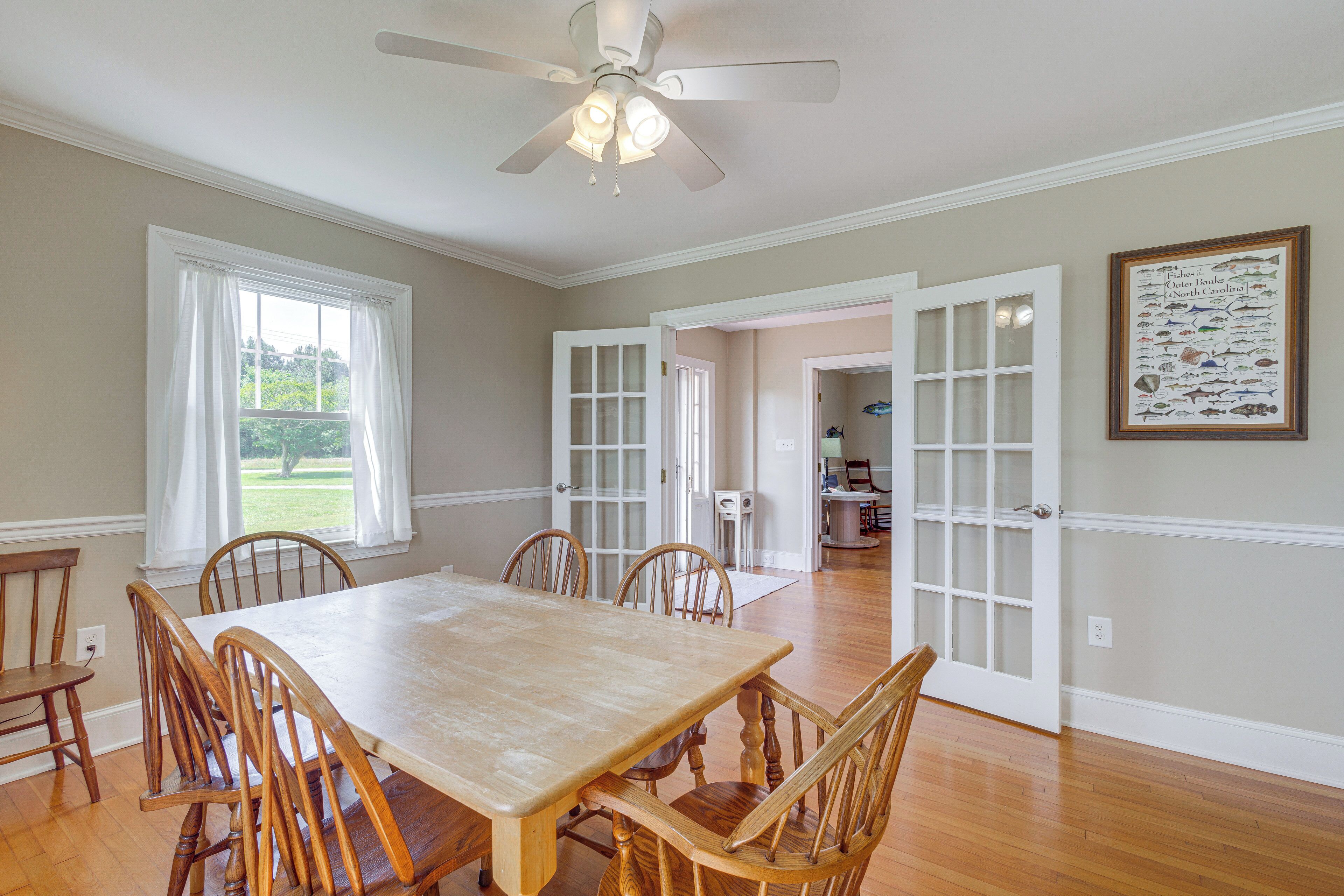 A dining room with a wooden table and chairs, a ceiling fan, and a framed fish illustration on the wall.