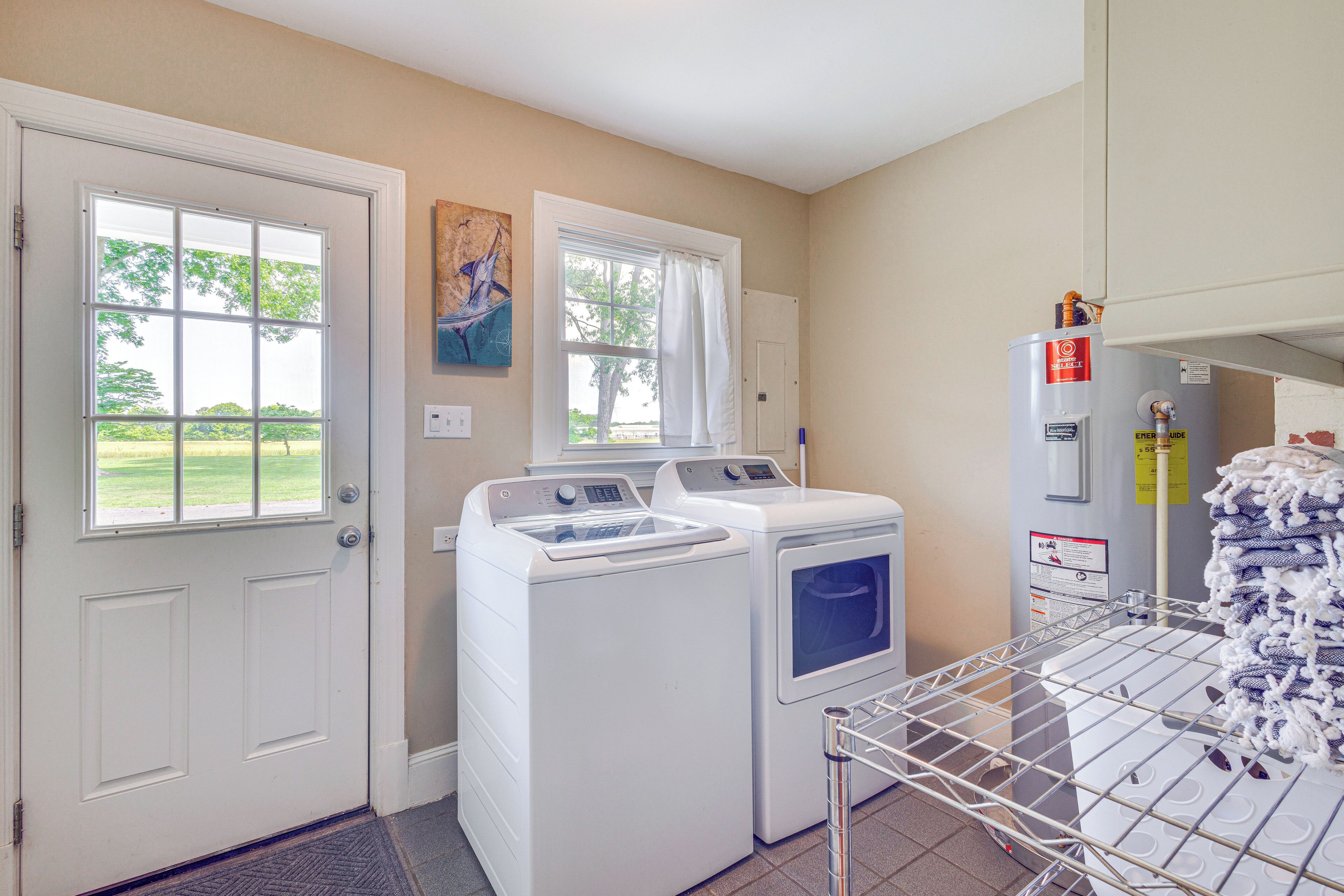 A laundry room with two front-loading washers and dryers, a drying rack, and a water heater.