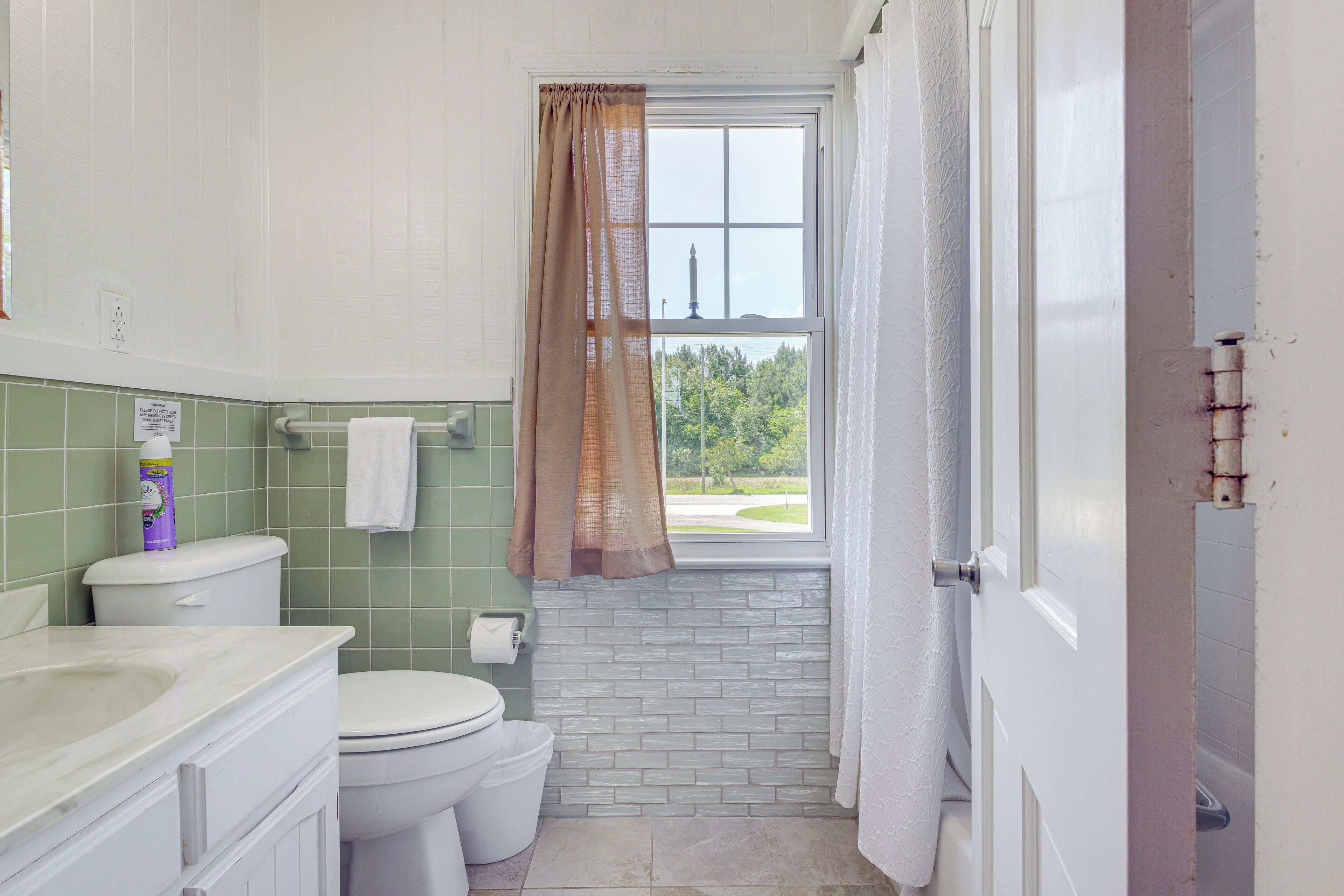 Une salle de bain équipée de toilettes, d’un lavabo et d’une fenêtre donnant sur un espace verdoyant.