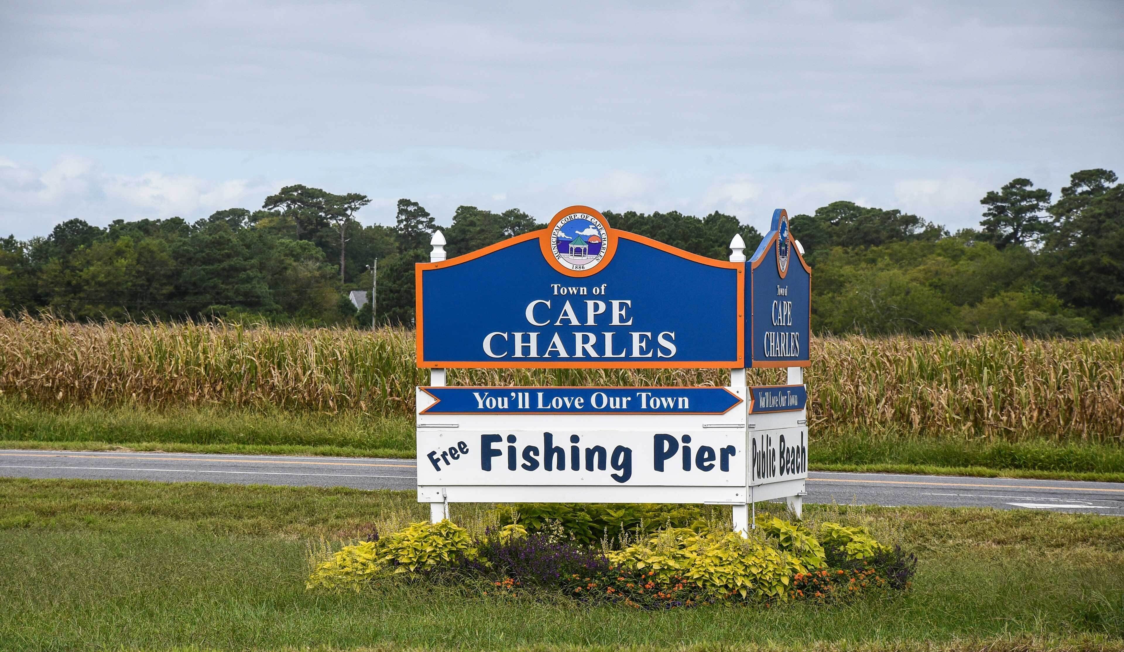Un letrero de bienvenida a Cape Charles, con un muelle de pesca y una playa pública.